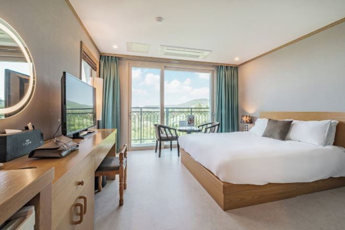 Une chambre d’hôtel avec un lit, un bureau avec un ordinateur, une chaise et un balcon avec vue.
