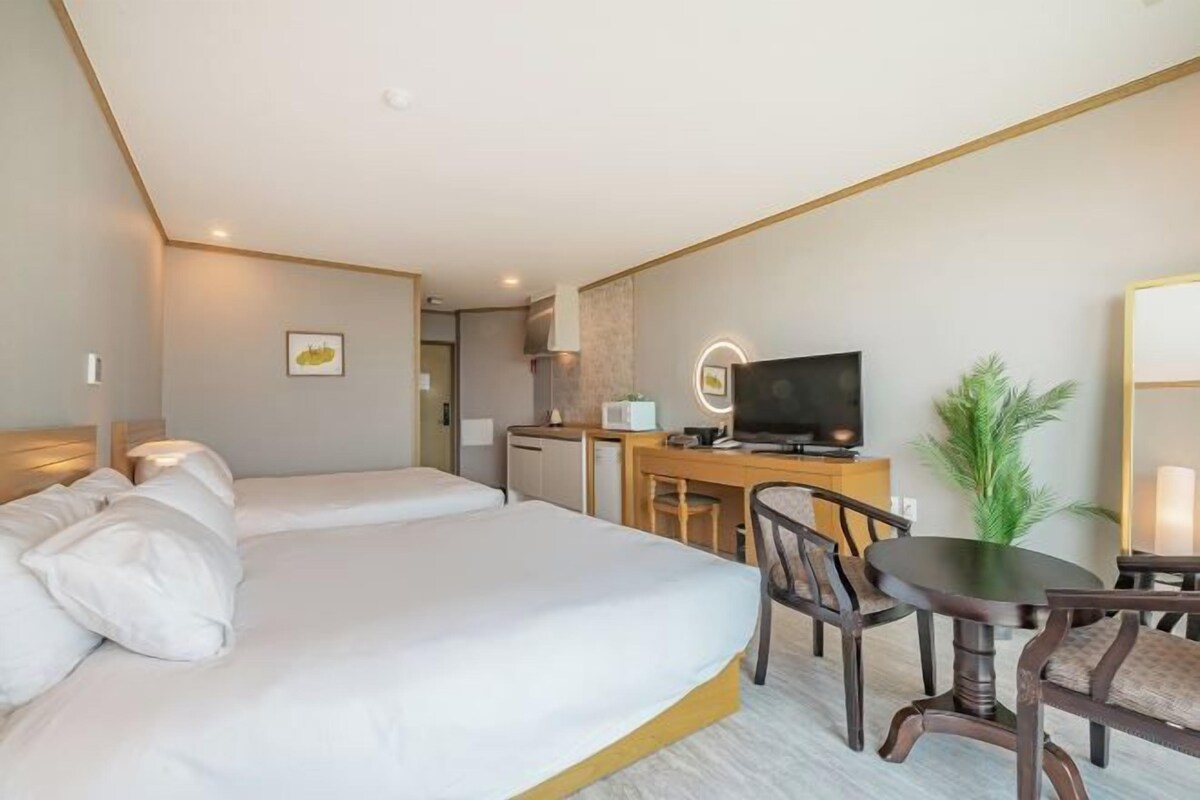 Une chambre d’hôtel avec deux lits, un bureau avec une télévision et une petite kitchenette.