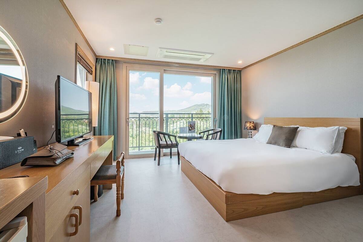 Een hotelkamer met een bed, bureau, stoel en een balkon met uitzicht.
