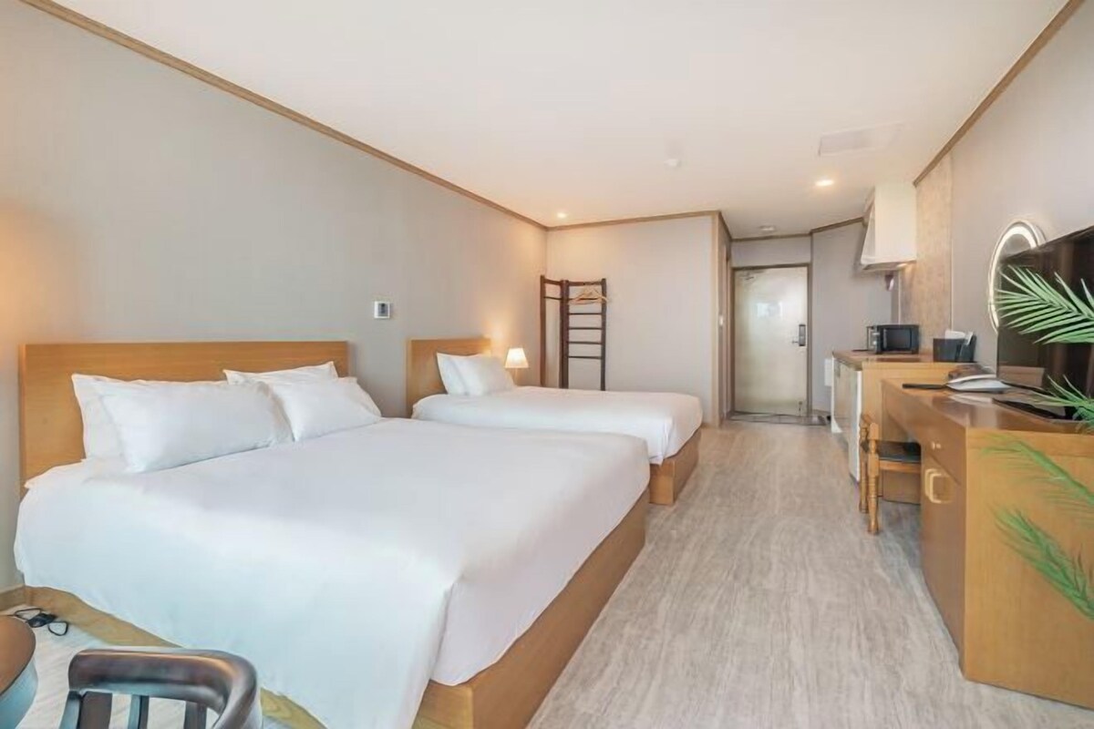 Una camera d'albergo con due letti, una scrivania, una sedia, uno specchio e un angolo cottura.