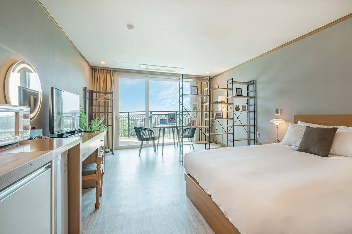 Een hotelkamer met een groot bed, een bureau met een computer, een stoel, een balkon met uitzicht en een plank met foto's.