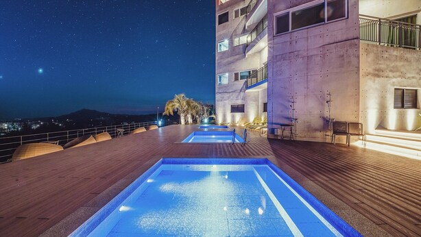 Una piscina en la azotea con un cielo nocturno despejado, vista de la ciudad y un edificio con balcones.