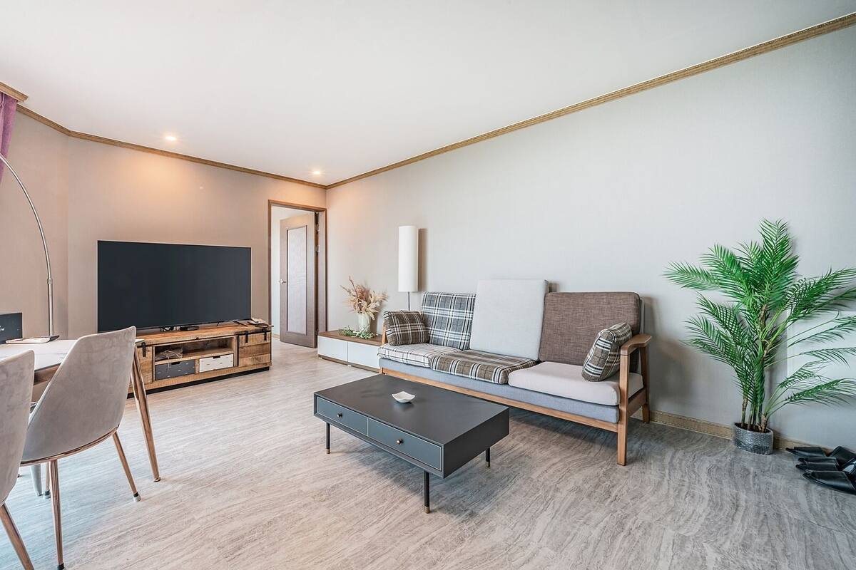 Een moderne woonkamer met een bank, salontafel, televisie en een eethoek met stoelen.