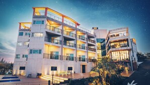 Un hotel de varios pisos con balcones, zona de piscina y una entrada bien iluminada.
