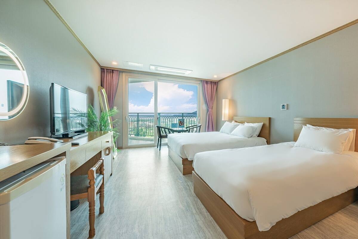 Hotelkamer met twee bedden, een bureau met televisie, een balkon met uitzicht en een lampje op het nachtkastje.