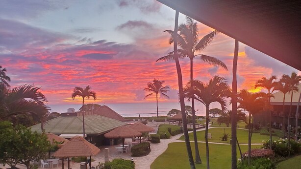 A resort with a pathway leading to a seating area, surrounded by palm trees and a view of the sunset. - KAUA'I BEACH RESORT-BEACHFRONT, OCEAN VIEW, POOLSIDE VIEW FROM YOUR LANAI (Lihue)