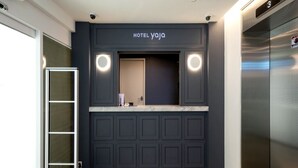 A modern hotel reception area with a dark wood panel design, a marble counter, and a visible elevator. - Hotel Yaja Gwangalli (Busan)