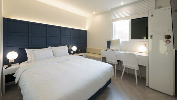 A hotel room with a large bed, bedside tables with lamps, a desk with a chair, and a refrigerator. - Hotel Yaja Gwangalli (Busan)