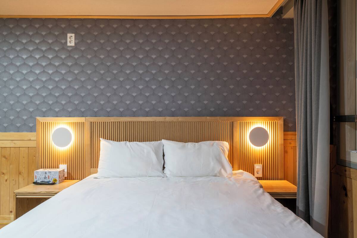 Ett hotellrum med en säng, två sängbord, en rund vägglampa och en sänggavel i trä.