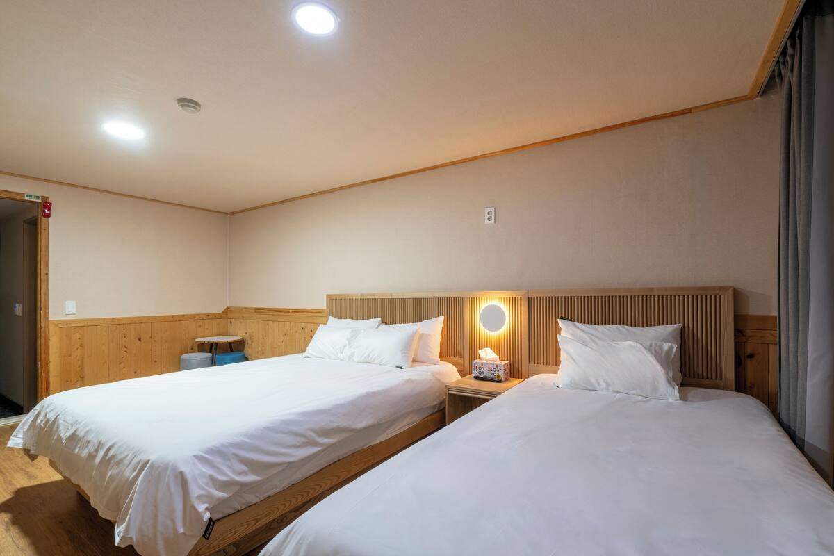 Ett hotellrum med två sängar, trägavlar, en rund väggklocka och ett litet bord.