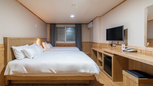 Une chambre d’hôtel avec un lit en bois, une télévision, un bureau avec un téléphone et une fenêtre avec des rideaux.