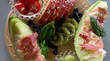 Tábua de madeira com frutas fatiadas, queijo e uvas.