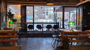 L’intérieur d’un restaurant donnant sur la rue, avec des tables et des chaises disposées pour accueillir les clients, et un luminaire décoratif suspendu au-dessus de l’entrée.
