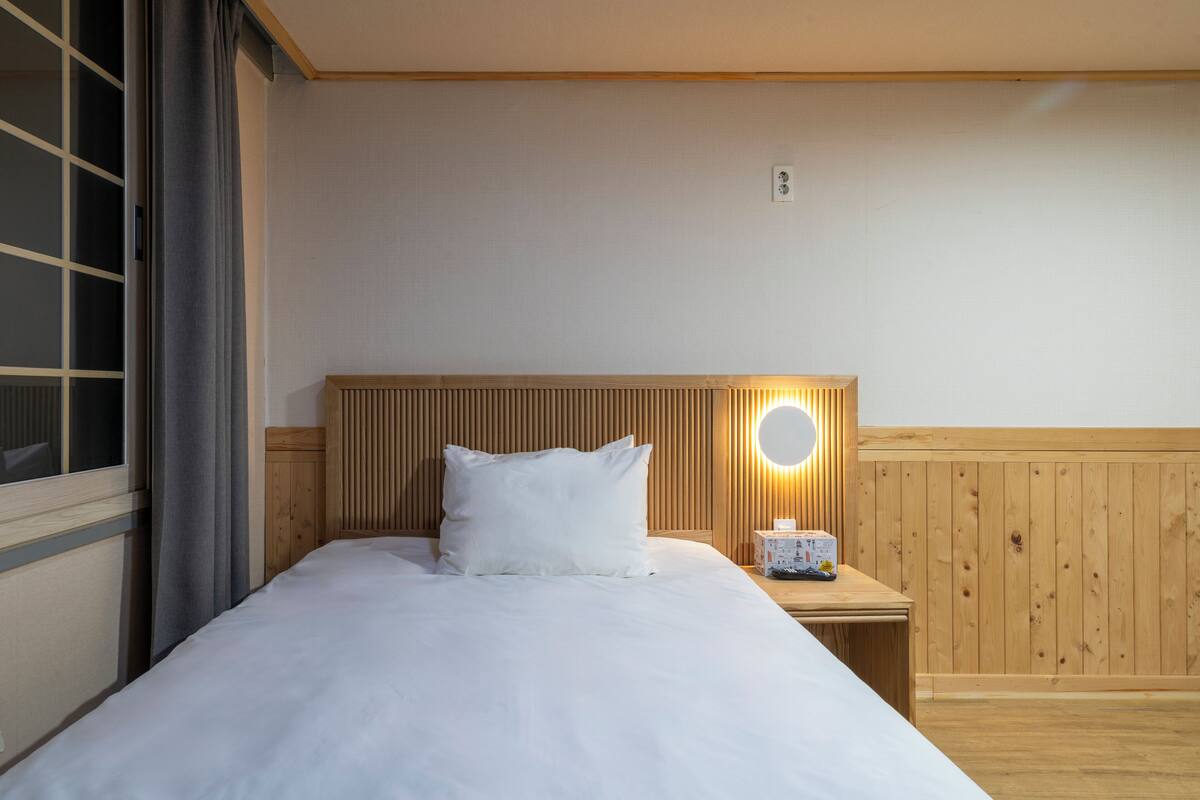 Ett hotellrum med en sänggavel i trä, ett nattduksbord med en lampa och ett fönster med gardiner.