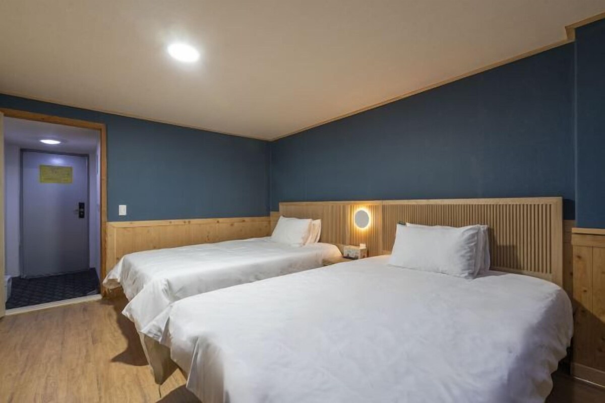 A hotel room with two beds, a wooden headboard, a nightstand, and a door with a sign.