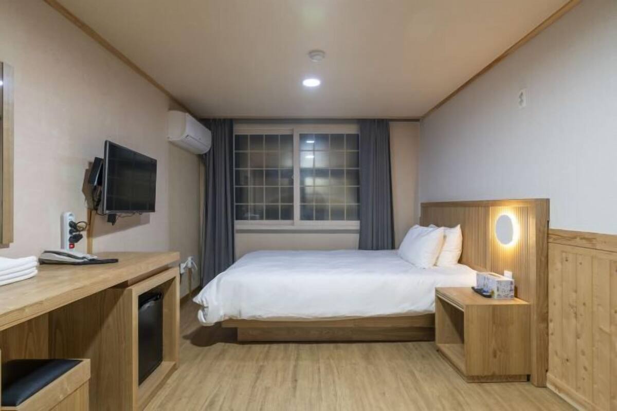 Ett hotellrum med en säng, ett skrivbord, en tv och ett nattduksbord med en lampa.