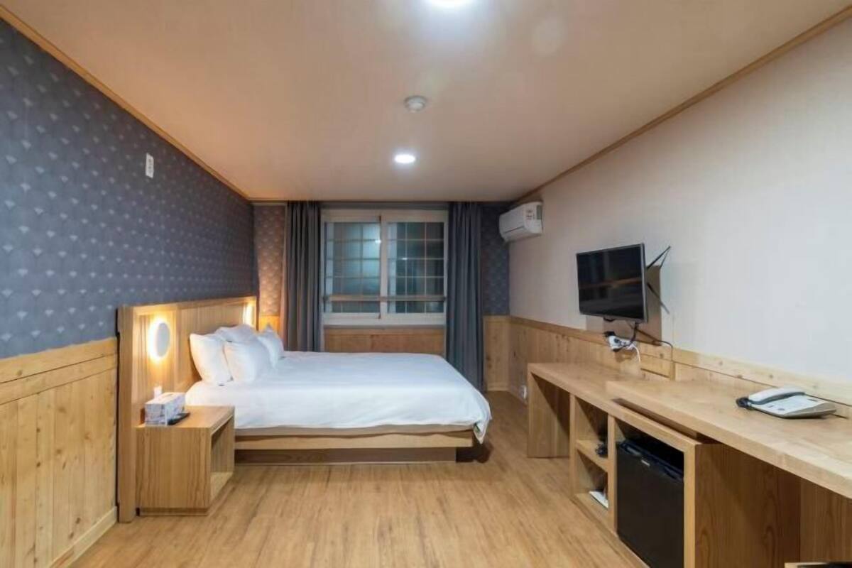 Ett hotellrum med en säng, ett nattduksbord, en tv och ett skrivbord med en stol.