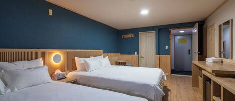 Habitación de hotel con dos camas, cabecero de madera, mesita de noche con lámpara, una pequeña mesa redonda, escritorio de madera y espejo.