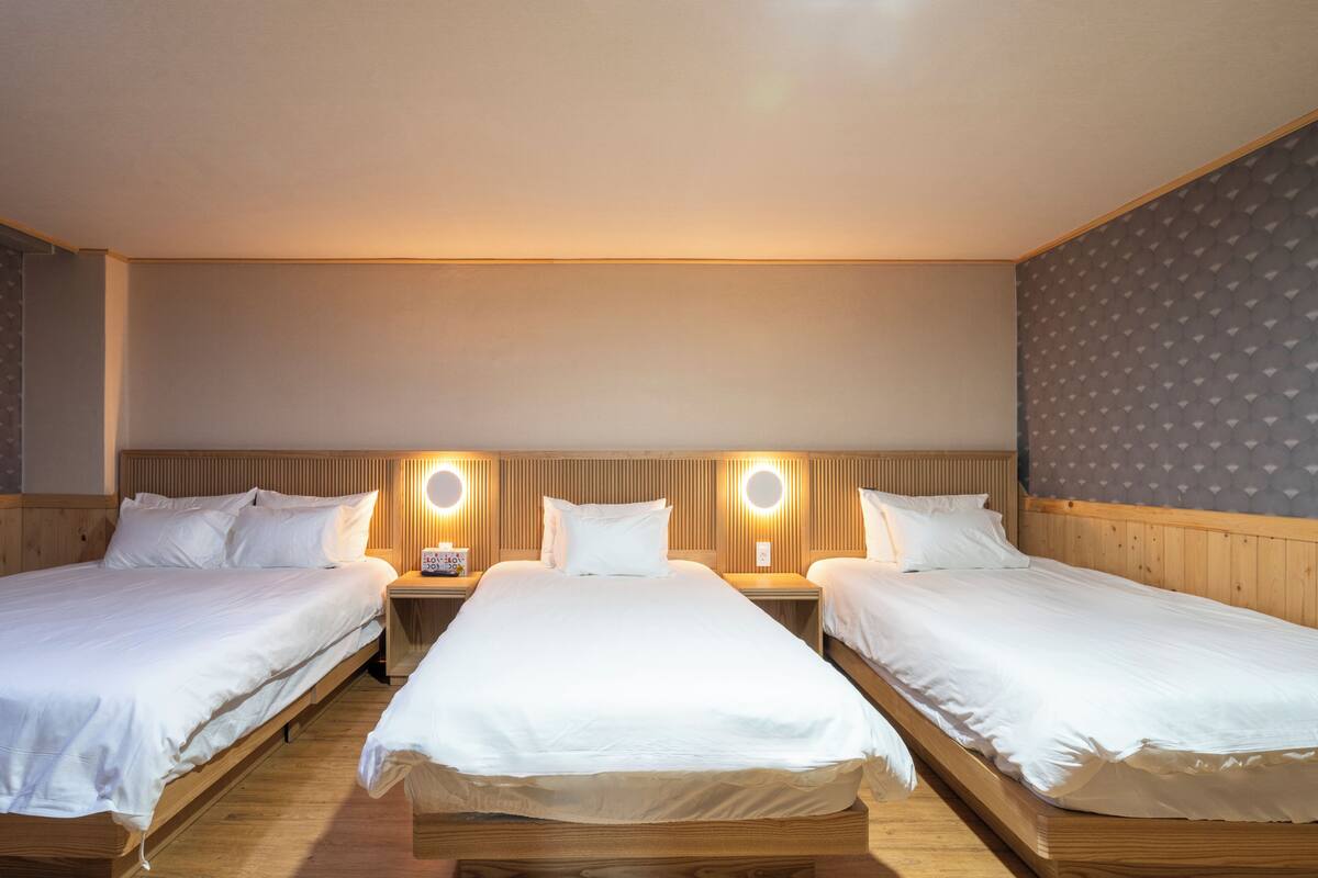 Ett hotellrum med tre separata sängar, trägavlar och runda vägglampor.