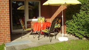 Eine Terrasse im Freien mit Tisch und vier Stühlen, einem gelb-weiß gestreiften Sonnenschirm und einer Backsteinmauer.