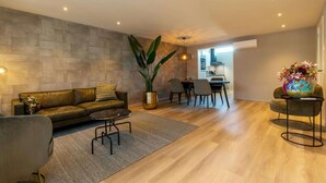 A modern living room with a leather sofa, a coffee table, a dining area with chairs, and a kitchen in the background.