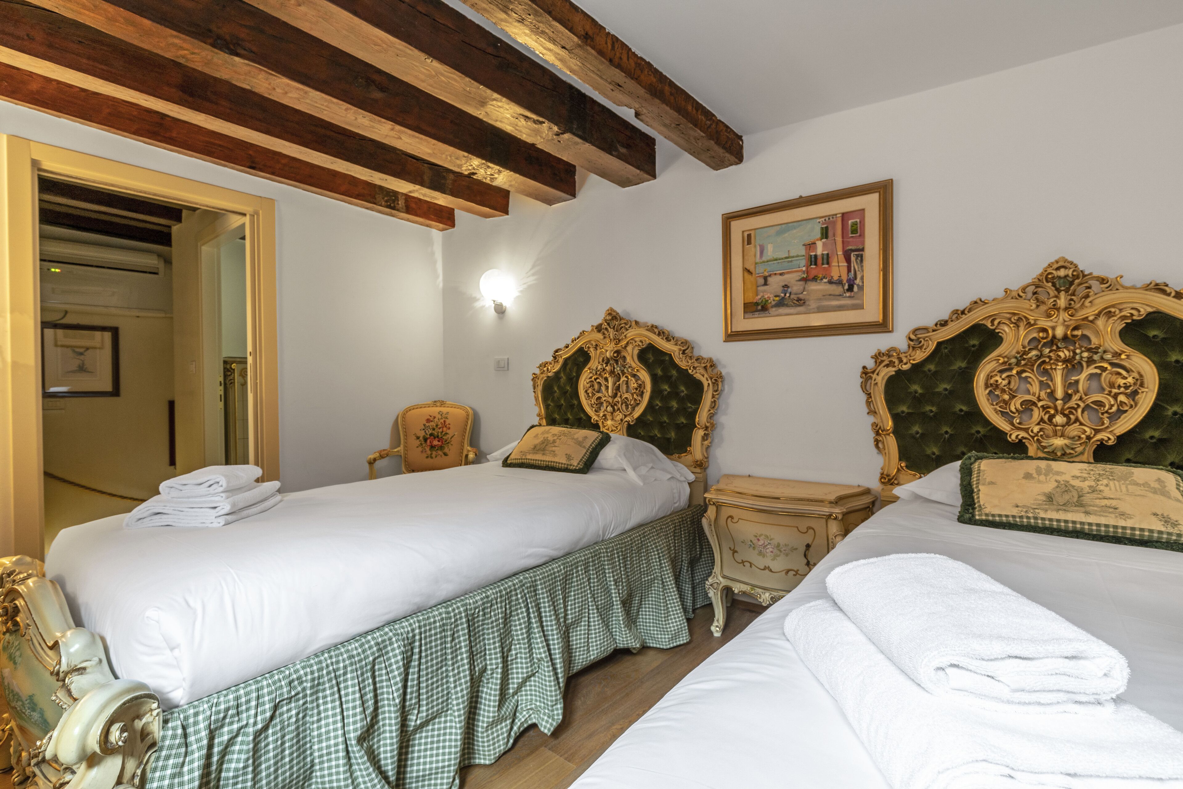 Habitación de hotel con dos camas, techo de madera, un cuadro en la pared y una mesita con lámpara.