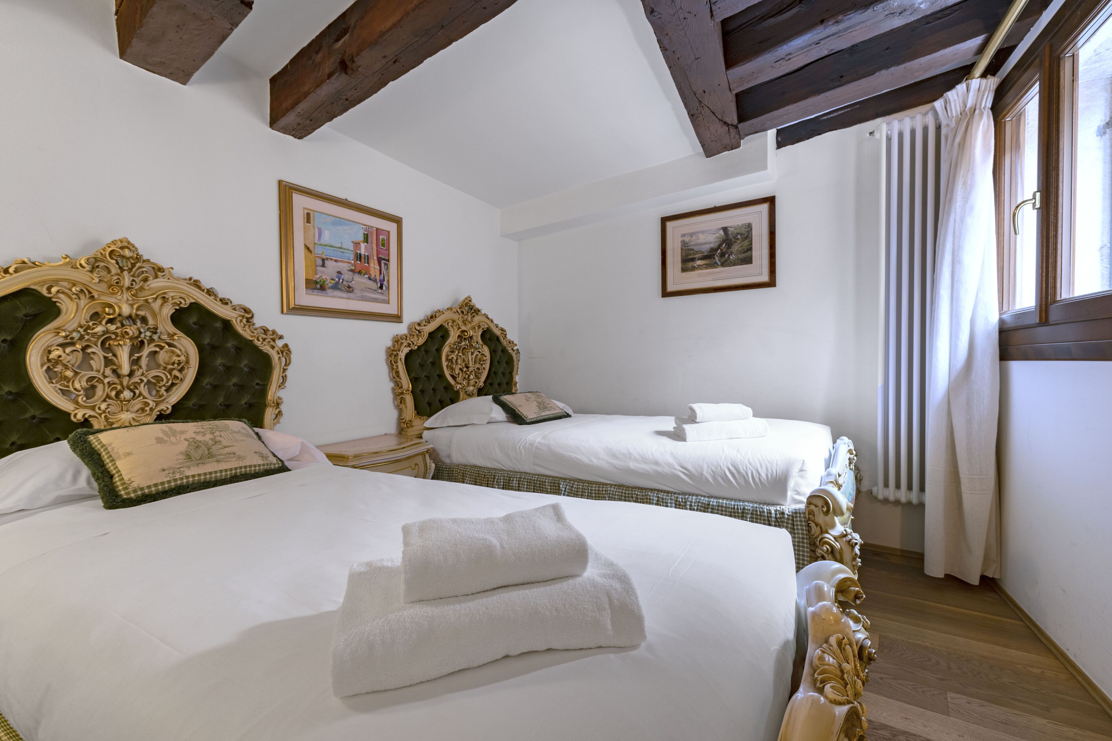 A hotel room with two beds, each with ornate headboards and white linens.
