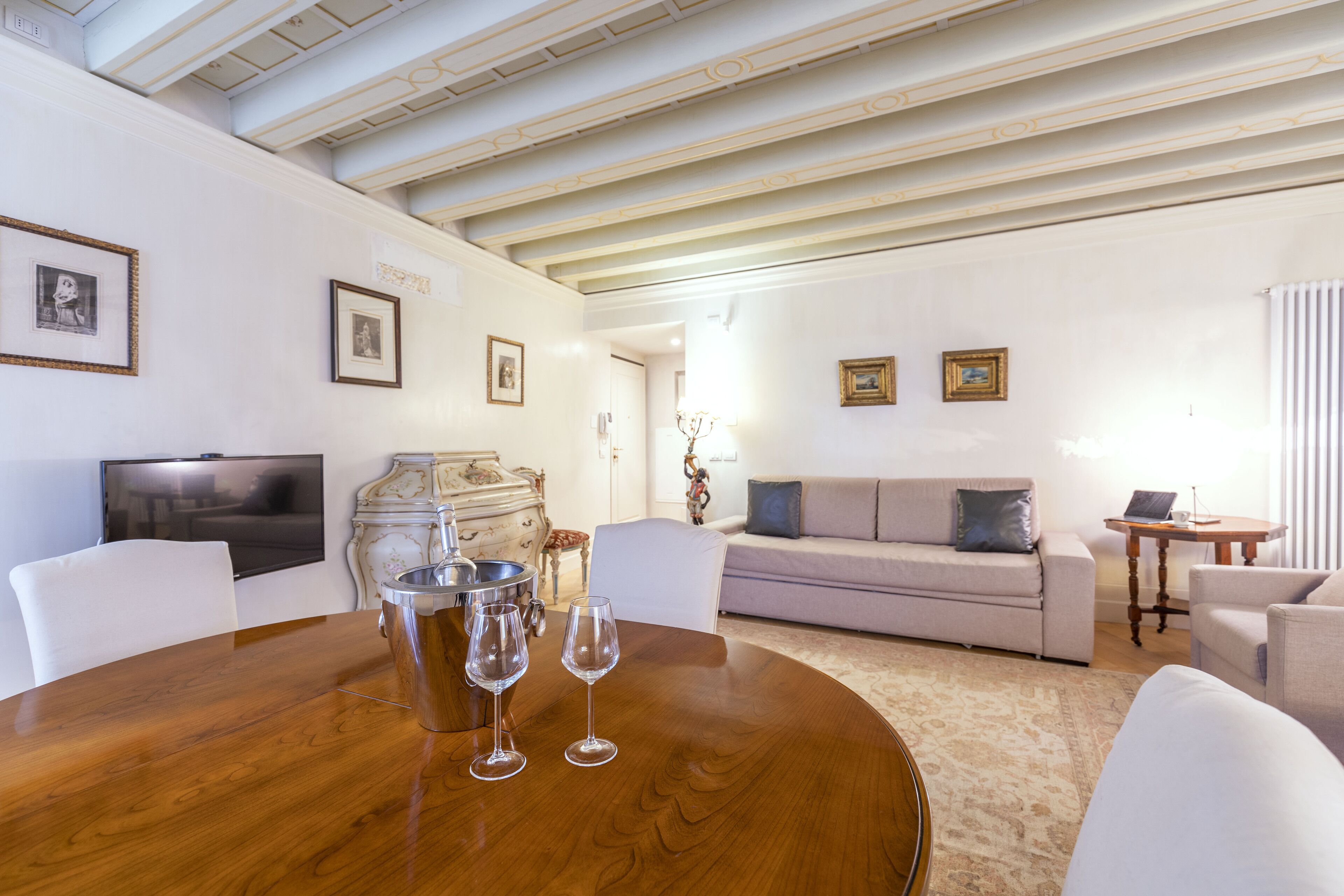 Een moderne woonkamer met een houten eettafel, witte banken en een flatscreen televisie.