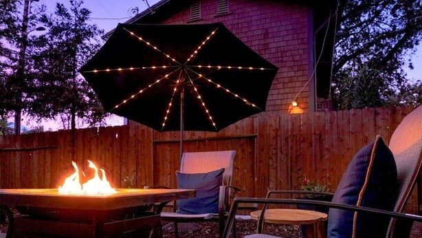 Un patio con un hoyo para fuego, mobiliario exterior y una sombrilla decorativa con luces.