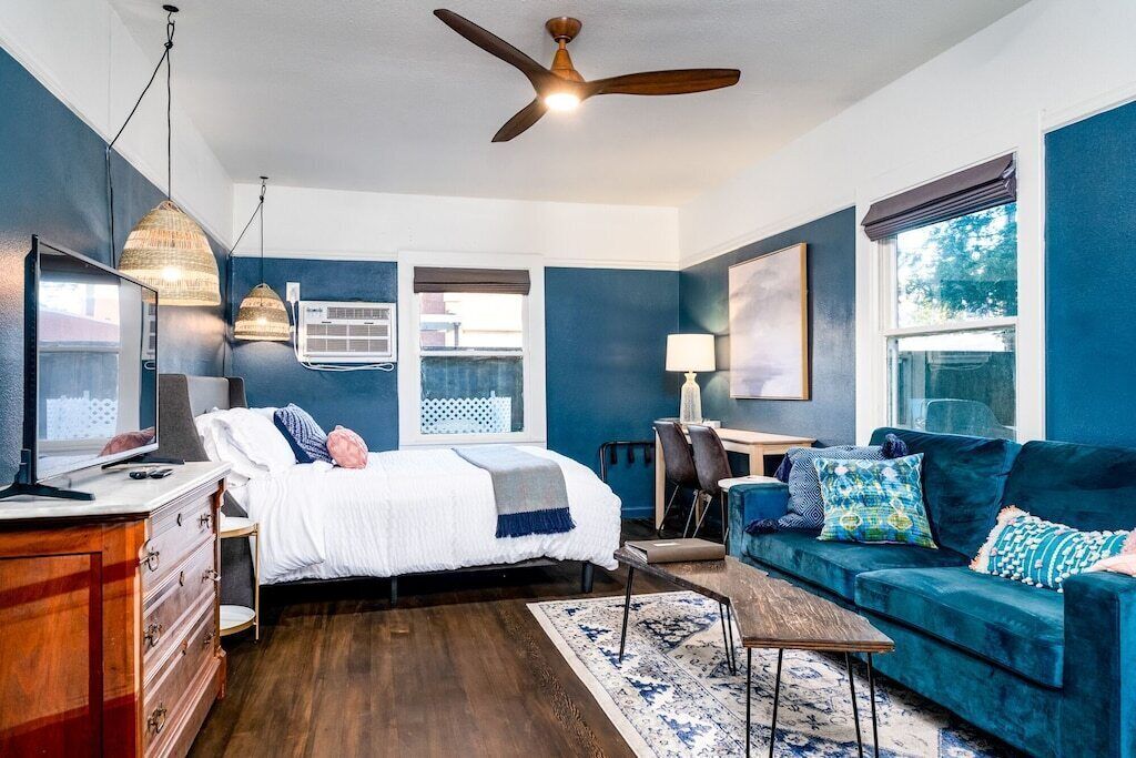 A bedroom with a bed, a blue couch, a desk, and a ceiling fan.