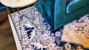Un sofá color turquesa con cojines estampados, una mesita redonda con un libro y una alfombra con diseño.
