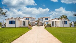 Une villa dotée d’une arche centrale, de nombreuses pièces avec des volets bleus et d’une pelouse bien entretenue.