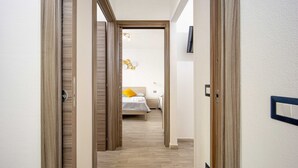 Un couloir menant à une chambre à coucher équipée d’un lit, d’une table de chevet et d’un luminaire fixé au mur.