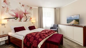 A hotel room with a bed, a TV, a desk, and a window with curtains. - FW 15, apartments on the beach - max. 4 persons - FeWo Am Strand / (Kühlungsborn)