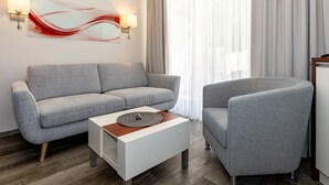 A modern living room with a grey sofa, a white coffee table, and a grey armchair. There is a wall-mounted artwork and two wall sconces. - FW 15, apartments on the beach - max. 4 persons - FeWo Am Strand / (Kühlungsborn)