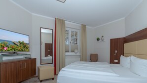A hotel room with a bed, a TV, a mirror, a window, and a small shelf. - FW 18, apartments on the beach - max. 4 persons - FeWo Am Strand / (Kühlungsborn)