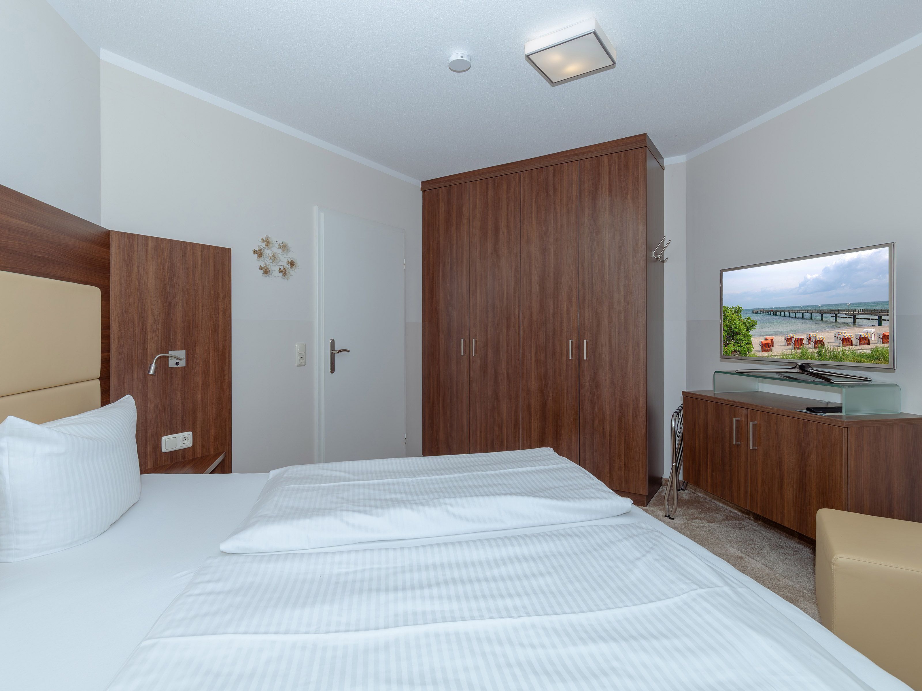 Ein Hotelzimmer mit Bett, Fernseher, Holzschrank und Blick auf einen Strand.