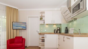 A compact kitchen with white cabinets, a microwave, a coffee maker, and a red chair. - FW 19, apartments on the beach - max. 4 persons - FeWo Am Strand / (Kühlungsborn)