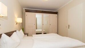 A hotel room with a large bed, a wardrobe, a bedside table, and a wall-mounted lamp. - FW 19, apartments on the beach - max. 4 persons - FeWo Am Strand / (Kühlungsborn)