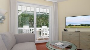 Una sala de estar con un sofá, una mesa de vidrio, una televisión y vistas a un balcón con mobiliario exterior.