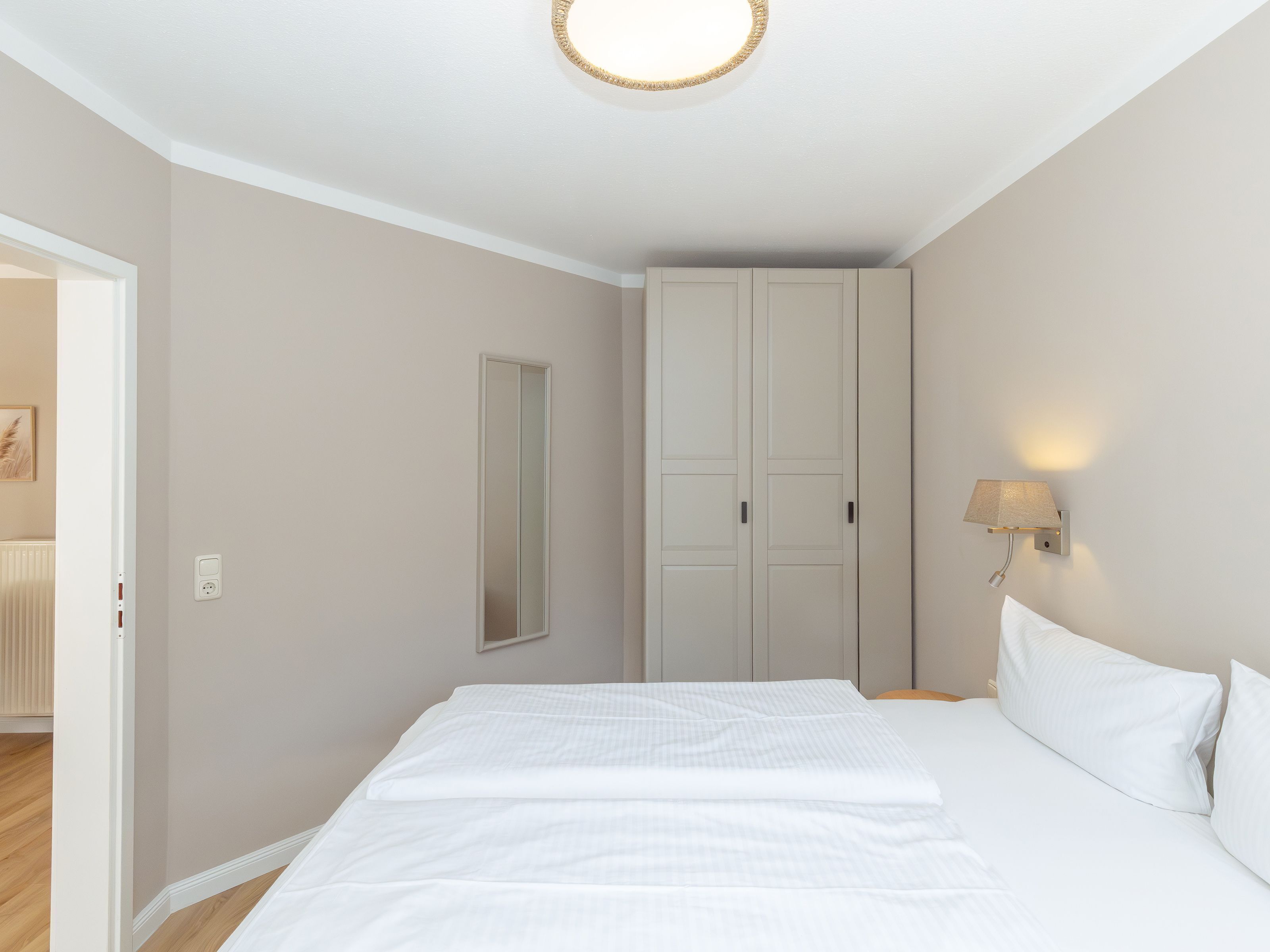 Ein Schlafzimmer mit einem Bett, einem Kleiderschrank, einer Wandleuchte und einer Tür zu einem weiteren Raum.