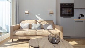 Ein modernes Wohnzimmer mit einem beigefarbenen Sofa, zwei Lampen und einem Esstisch mit einem Drahtkorb.
