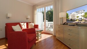 Una habitación con un sofá rojo estampado, una mesita redonda pequeña, un televisor sobre un mueble bajo y un ventanal corredizo que da a un espacio exterior.