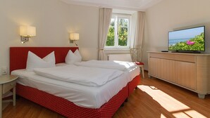 Una habitación de hotel con cama, televisión, mesita de noche y ventana con cortinas.