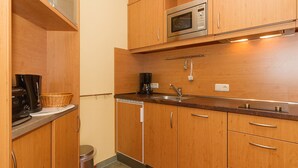 Een kleine keuken met houten kastjes, een RVS spoelbak, een magnetron en een koffiezetapparaat.