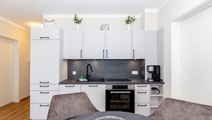 Eine moderne Küche mit weißen Schränken, einer schwarzen Arbeitsplatte, einem eingebauten Backofen und einem Esstisch mit zwei Stühlen.