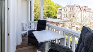 Ein Balkon mit Tisch und Stühlen, Blick auf Gebäude und eine Holzterrasse.