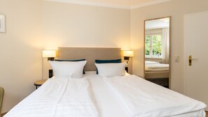 Ein Hotelzimmer mit einem großen Bett, zwei Nachttischen mit Lampen, einem Spiegel und einem Fenster mit Vorhängen.