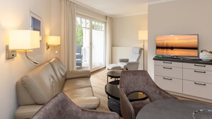 Ein modernes Wohnzimmer mit einer Couch, Sesseln, einem Couchtisch und einem Fernseher auf einem Schrank.