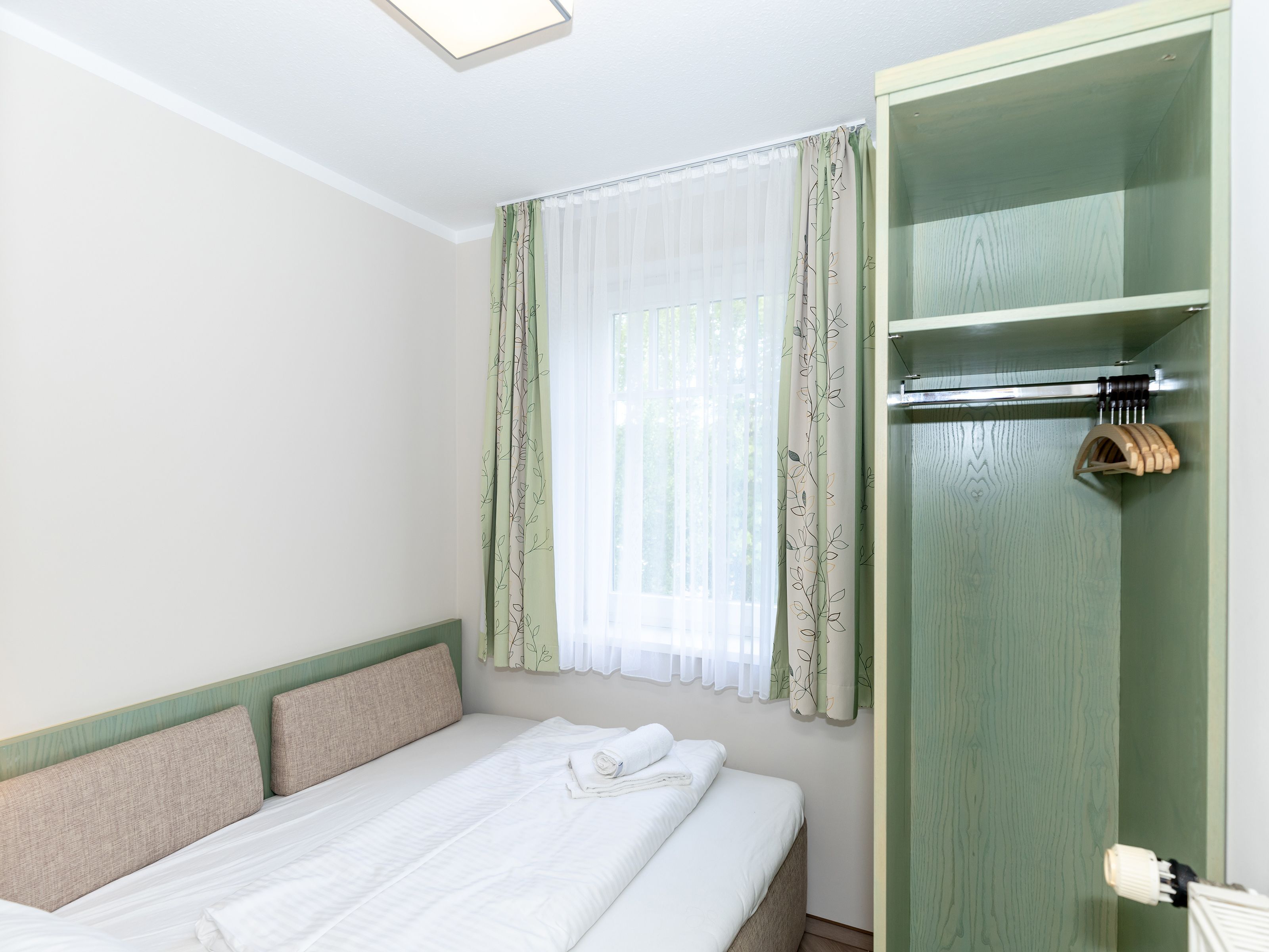 A bedroom with a bed, a wardrobe, and a window with curtains.